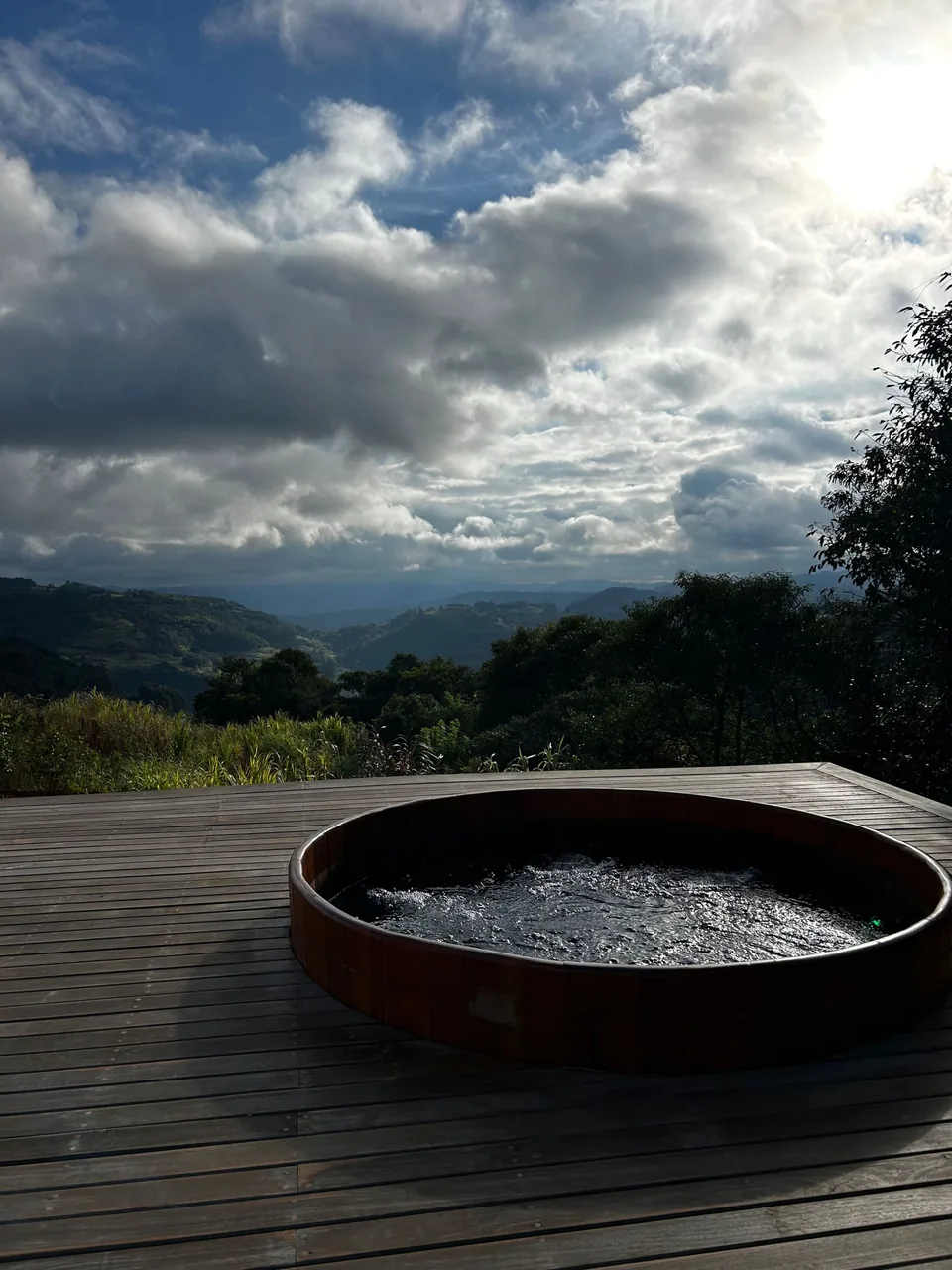 Ofurô de madeira no deck, com as nuvens e os morros ao fundo